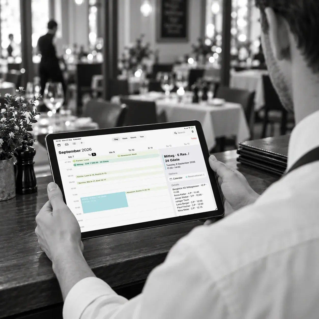 Illustrative Restaurantszene: Blick über die Schulter auf einen Tablet-Kalender mit anonymisierten Reservationen und Schichten